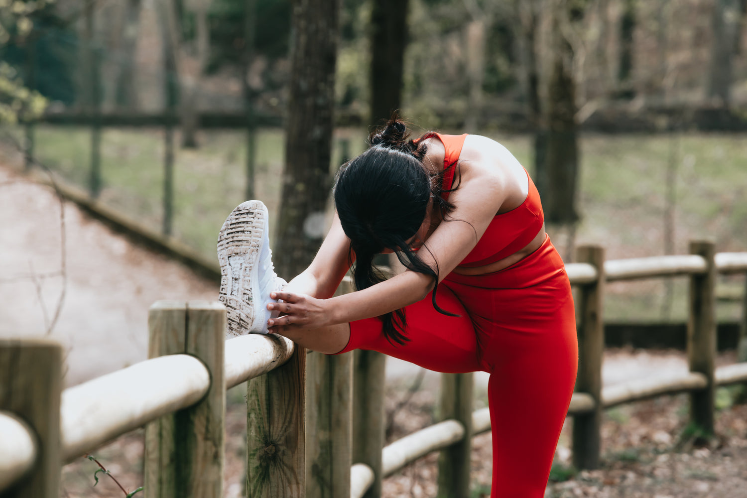 a-woman-stretches-outdoors-against-a-wooden-fence - Simply Conveniently